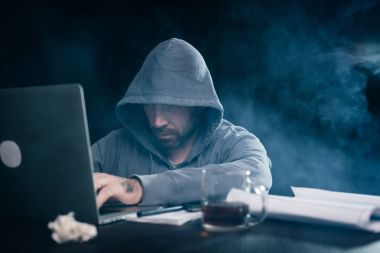 gizemli sakallı adam yüzünü başlık altında gizler, laptop karanlıkta kesmek