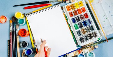 mavi bir masada sanatsal aksesuarları, suluboya ve guaş, birçok fırçaları vardır