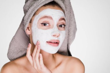 güzel bir genç kız kendini önemser, beyaz bir besleyici maske yüzünde bir spa yordam koymuştur