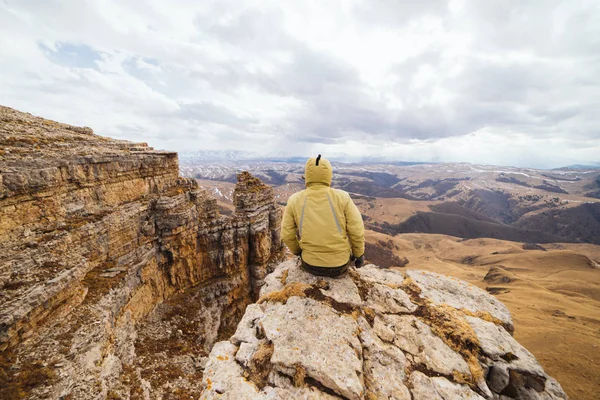 A male traveler sits on the edge of a cliff and enjoys mountain clean air — Stock Photo, Image