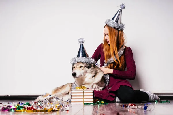 Молодая рыжая девушка, сидящая на полу со своей большой собакой, празднующей Новый год — стоковое фото