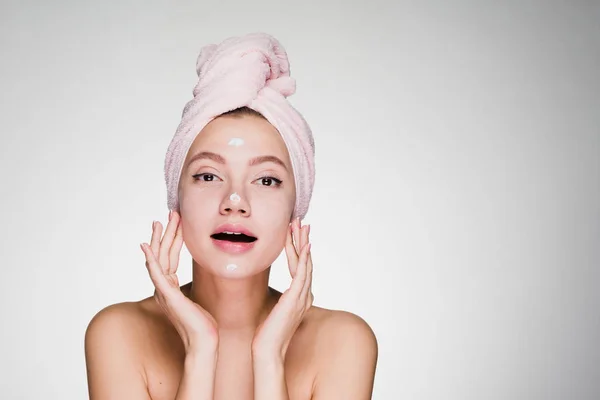 Young attractive girl with pink towel on her head applying moisturizer on face — Stock Photo, Image