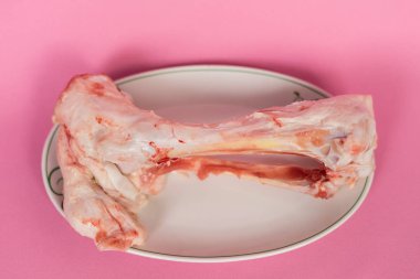 Beyaz bir tabak pembe bir yüzey üzerinde bir kemik etli yatıyor