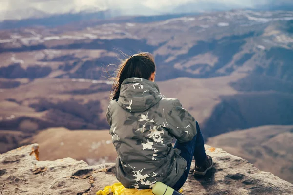 Молода активна дівчина сидить на краю скелі і насолоджується гірським повітрям — стокове фото