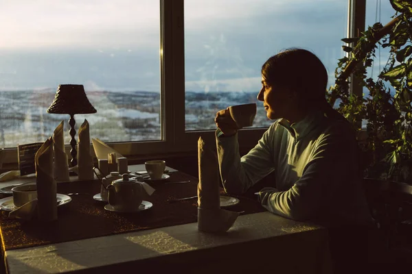 Una joven se sienta en un café y bebe té aromático caliente, mira por la ventana y disfruta —  Fotos de Stock