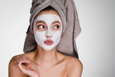 Kafasındaki bir havlu ile sürpriz bir genç kız beyaz bir besleyici maske yüzüne karşı uygulanan.