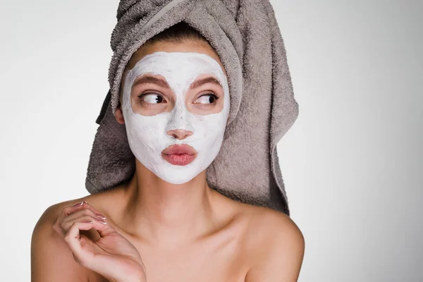 Ein überraschtes junges Mädchen mit einem Handtuch auf dem Kopf trug eine weiße nahrhafte Maske über ihr Gesicht — Stockfoto