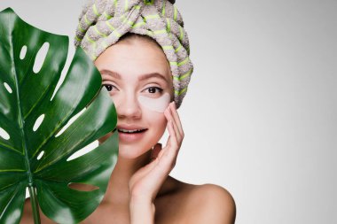 Holding bir yaprak yeşil, gün spa çekici gülümseyen kız beyaz lekeler, gözleri altında kafasındaki bir havlu ile