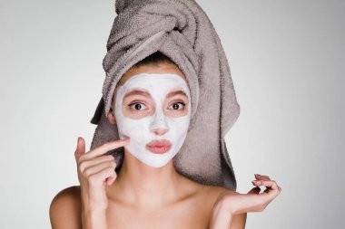 Kafasındaki bir havlu ile sürpriz bir genç kız beyaz bir besleyici maske yüzüne karşı uygulanan.