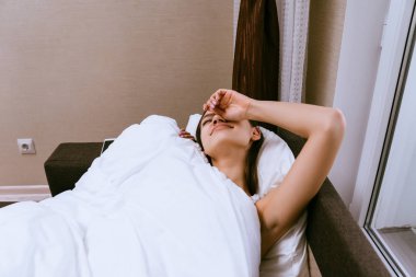 uykulu genç kız beyaz bir battaniye altında yatakta yatıyor, kalkmak istemiyor