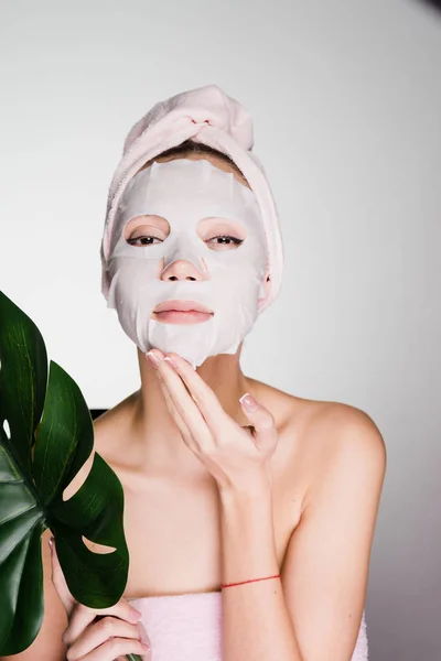 Young beautiful girl with a pink towel on her face tissue moisturizing mask, day spa — Stock Photo, Image