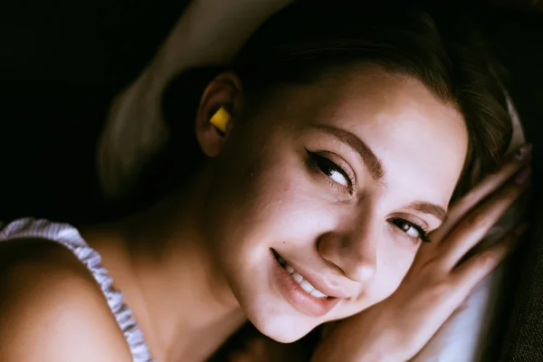 Boldog fiatal lány megy az ágyba, a füle utcai zajtól sárga füldugók — Stock Fotó