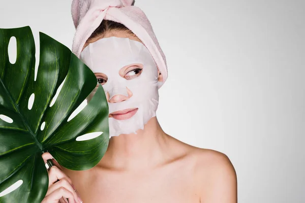 Giovane ragazza con un asciugamano rosa sulla testa, sul viso una maschera idratante tessuto, day spa — Foto Stock