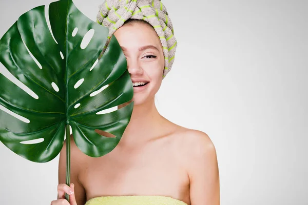 Szczęśliwy uśmiechający się dziewczyna z ręcznikiem na głowie posiada zielony liść, day spa — Zdjęcie stockowe