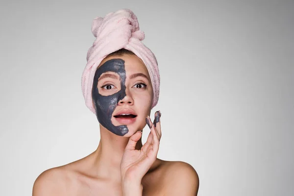 Egy szép meglepett lány a fején rózsaszín törülközővel alkalmazott agyagos maszk — Stock Fotó