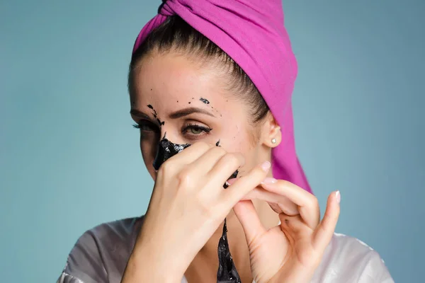 Giovane ragazza con un asciugamano rosa sulla testa, rimuove una maschera nera dal suo viso — Foto Stock