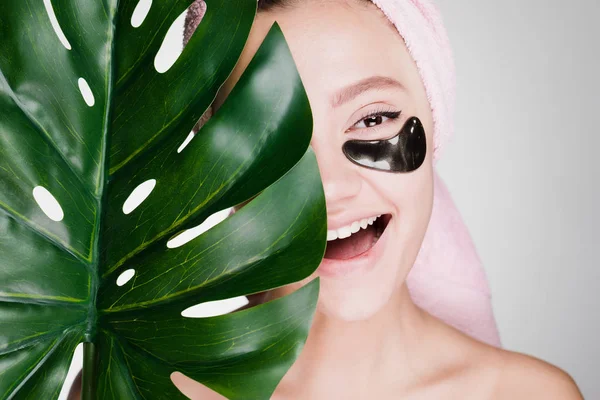 Menina sorridente feliz com uma toalha na cabeça segurando uma folha verde, spa dia, sob os olhos manchas pretas — Fotografia de Stock