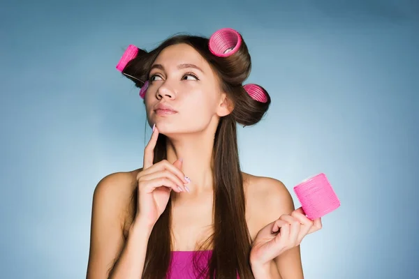 Une jeune fille pense à une coiffure à la mode, sur sa tête un gros bigoudi rose — Photo