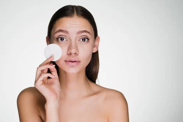 A cute young girl looks after the skin on her face, holds a white cotton pad to cleanse the skin on her face — Stock Photo, Image