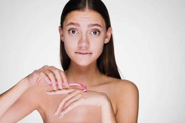 Молодая разочарованная девушка бреет руки розовой бритвой — стоковое фото
