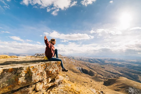 Aktif genç kız uçurumun kenarında oturur, dağ havası ve güneş sahiptir — Stok fotoğraf
