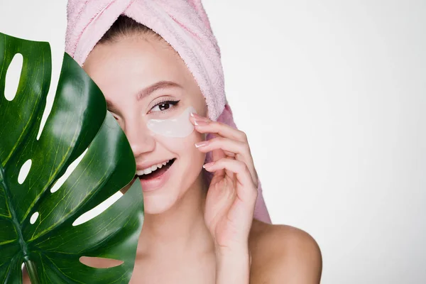 Happy young girl with a pink towel on her head, under the eyes of a patch, holds a green leaf, day spa — Stock Photo, Image