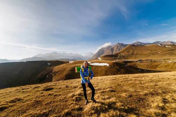 Активная молодая девушка в синей куртке путешествует по Кавказскому хребту с рюкзаком и палаткой — стоковое фото