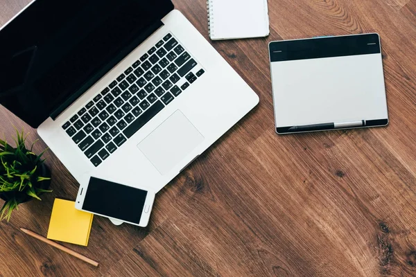 Op de houten vloer is een laptop voor werk, een grafisch tablet, een smartphone en een notebook — Stockfoto