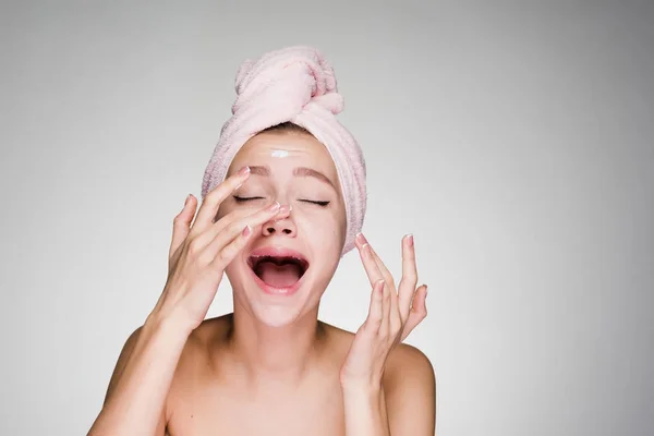 彼女の頭を彼女の顔に保湿剤を適用するピンクのタオルで面白い少女 — ストック写真