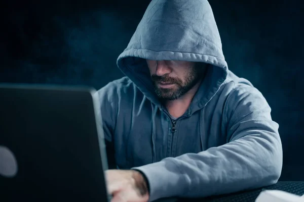 Misterioso barbudo homem esconde seu rosto sob o capô, hacks o laptop — Fotografia de Stock