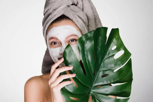 Grappige schattig meisje doet spa procedures, dragen handdoek op gezicht, voedende wit masker op het gezicht — Stockfoto