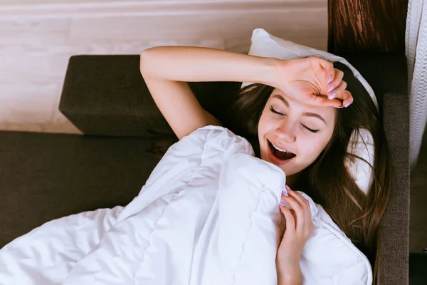 Nettes junges Mädchen am frühen Morgen aufgewacht, liegt im Bett unter einer weißen Decke — Stockfoto