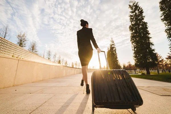 Confident slender woman stewardess in uniform goes on a flight with a suitcase in the rays of the sun — Stock Photo, Image