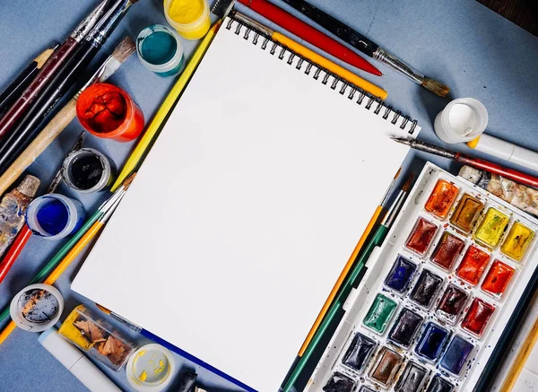 Mnoho nástrojů a barvy pro kreslení leží kolem prázdný Poznámkový blok — Stock fotografie