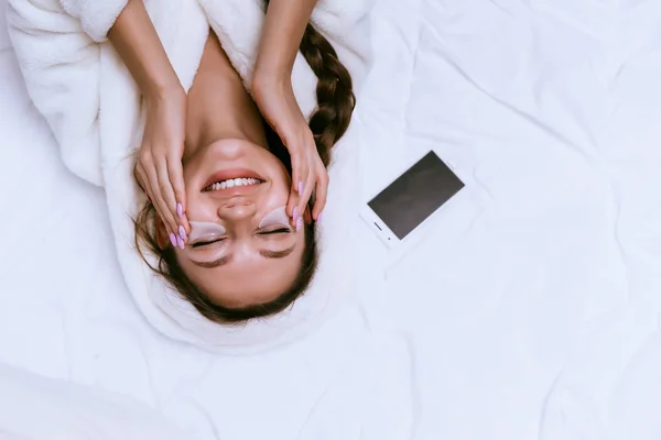 Dívka v bílém rouchu leží v posteli a úsměvy — Stock fotografie