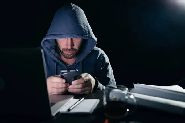 노트북에서 작업 하는 경험 있는 해커는 전화에 뭔가 확인 — 스톡 사진