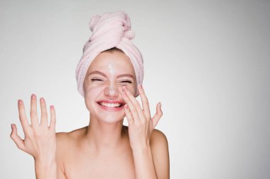 Yüzünde bir Besleyici krem uygulamak başında genç kız pembe havlu ile gülüyor