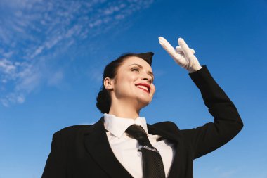 uçak için bekleyen mutlu gülümseyen kadın hostes üniformalı gökyüzüne doğru baktı