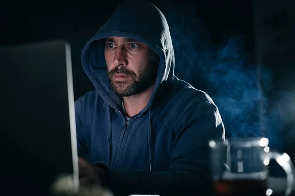 criminal adult man in hood hacking laptop in the dark