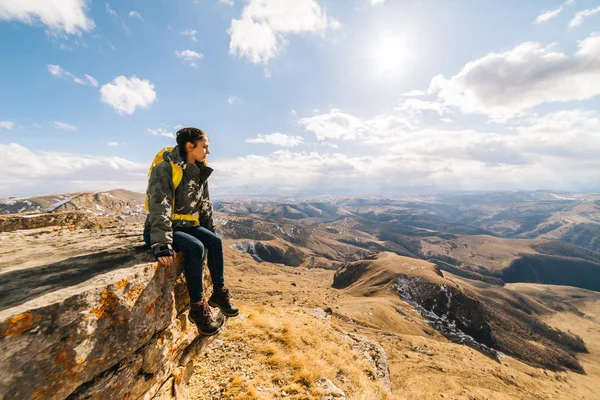 Fiatal nő utas ül a szélén a szikla, élvezi természet és a nap — Stock Fotó