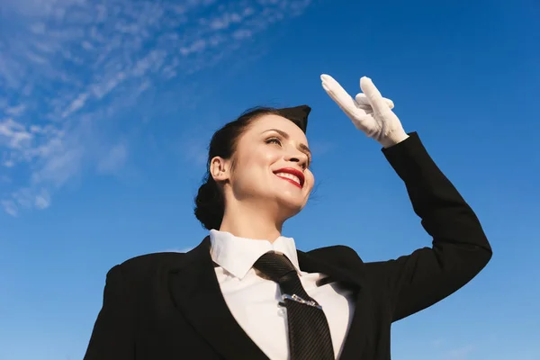 幸せの笑みを浮かべて女性スチュワーデス制服で見上げる空に飛行機を待っています。 — ストック写真