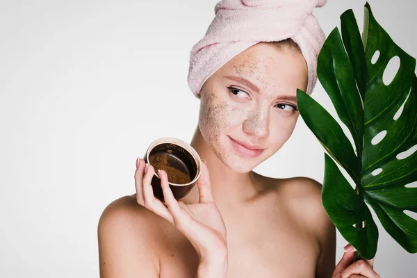 Linda menina com uma toalha rosa na cabeça aplicou uma esfoliação de café em seu rosto, procedimentos de spa — Fotografia de Stock