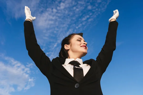 Glückliche junge Stewardess in Uniform hob unter blauem Himmel die Hände — Stockfoto