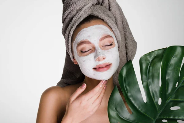 Lovely young girl with a towel on her head applied a white moisturizing mask on her face, day spa — Stock Photo, Image