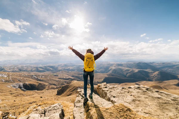 Active girl travels along the Caucasian ridge, with a yellow backpack, arms raised — Stock Photo, Image