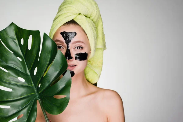Una linda jovencita con una toalla verde en la cabeza se aplicó una máscara de limpieza negra en las áreas problemáticas de su cara — Foto de Stock