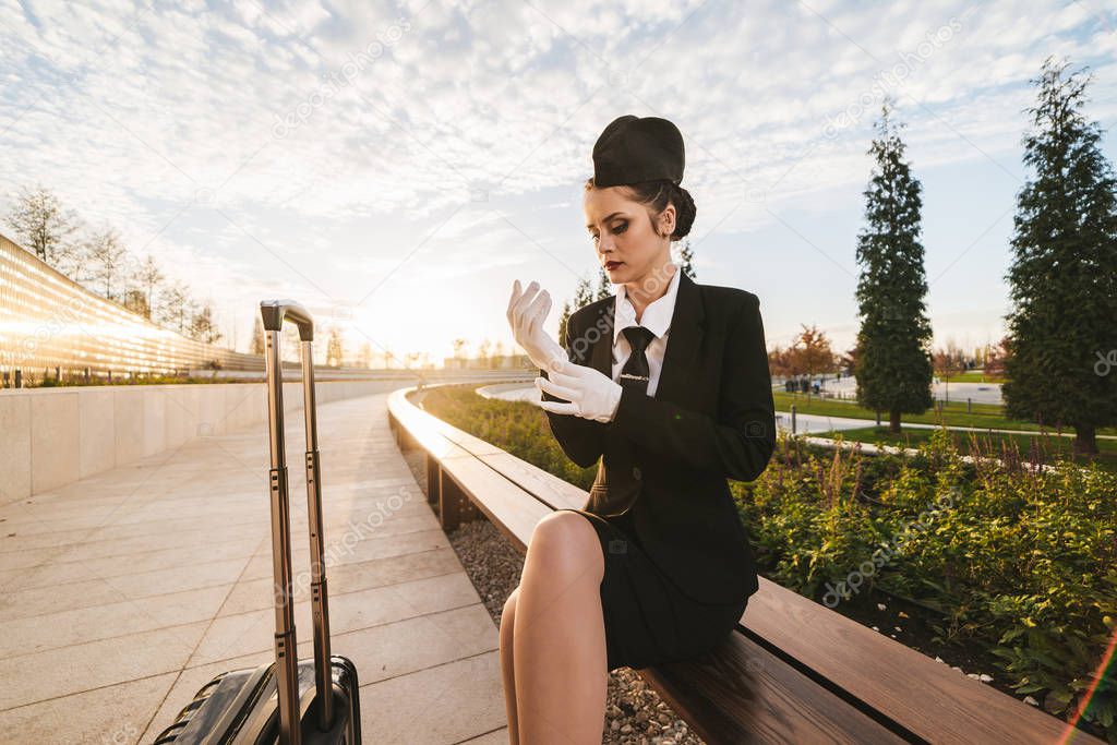 pensive young woman stewardess in uniform waiting for flight, with suitcase