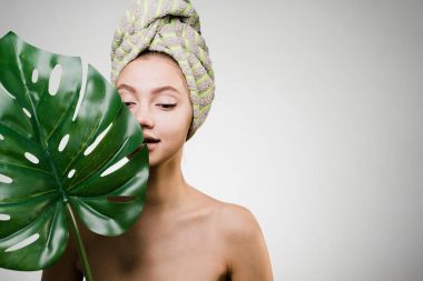 Kafasındaki bir havlu ile genç çekici kız tutan bir yaprak yeşil, gün spa