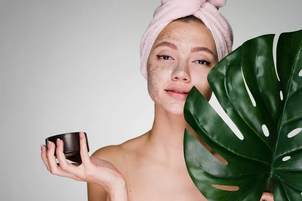 attractive young girl with a towel on her head applied a coffee scrub on her face, day spa