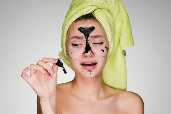 Sad young girl with a green towel on her head removes a black mask from her face — Stock Photo, Image